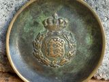 une vieille plaque en laiton ornée d'une couronne, posée sur une table en bois