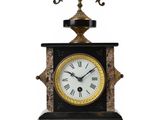 une horloge noire et dorée posée sur un socle, sur fond blanc