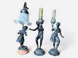 three figurines of a woman holding a lamp and a man holding a lamp