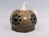 un vase marron percé de trous posé sur une surface blanche