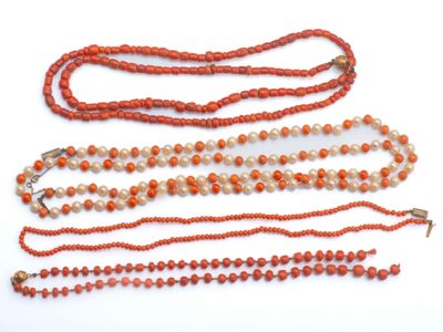 trois colliers composés de perles orange et blanches, posés sur une surface blanche