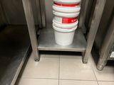 several buckets of food are stacked on a metal shelf in a kitchen