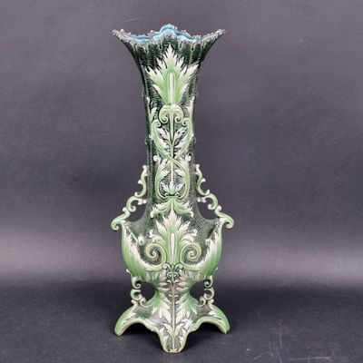 un vase vert et blanc posé sur une surface noire, avec un arrière-plan gris