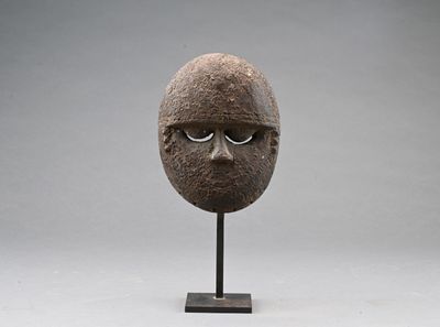 une sculpture représentant un visage, posée sur un socle, sur fond gris