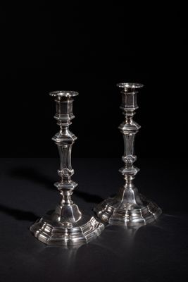 pair of silver candlesticks on a black surface with a black background