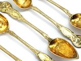 six cuillères en or aux motifs ouvragés sont alignées sur une surface blanche