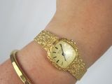 a woman ' s arm with a gold bracelet and a watch on it