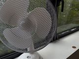un ventilateur posé sur le rebord d'une fenêtre, devant celle-ci