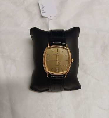une image représentant une montre en or posée sur un coussin noir, sur une surface blanche