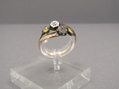 une bague en or sertie d'un diamant, posée sur un socle transparent