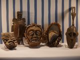 many wooden masks sitting on a table with a striped wall behind them