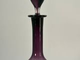 a purple glass bottle with a black top on a table