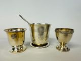 three silverplated cups and spoons on a white surface
