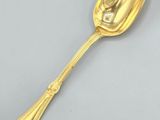 a gold spoon with a handle on a gray surface