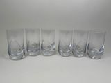 six verres à pied en verre transparent alignés sur une surface blanche