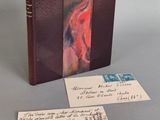 un livre à la couverture rouge posé sur une table, à côté d'une feuille de papier