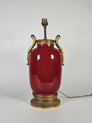 un vase rouge muni d'une anse dorée, posé sur une table blanche