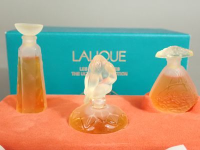 trois flacons de parfum posés sur une table, avec une boîte en arrière-plan