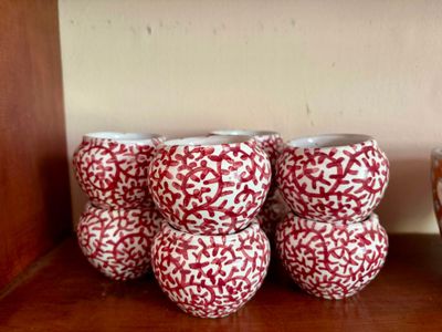 trois vases rouges et blancs posés sur une étagère en bois, à côté d'un bol