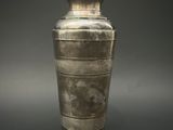 un vieux vase en argent posé sur une surface grise