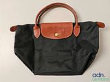 Le sac Longchamp est noir et possède une poignée marron.