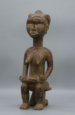 une vieille statue en bois représentant un homme assis sur un tabouret