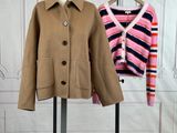 two coats on a stand in front of a white wall and a pink and blue striped sweater