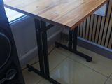 une table avec un plateau en bois et des pieds noirs, placée devant une fenêtre