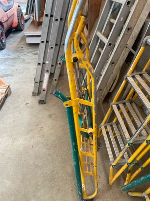 Des échelles jaunes et vertes sont empilées les unes à côté des autres dans un garage