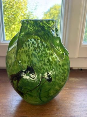 un vase vert posé sur une table en bois près d'une fenêtre