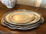 trois assiettes en argent posées sur une table en bois, avec un vase en arrière-plan