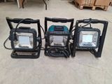 Trois lampes de travail portables sont posées par terre dans un entrepôt