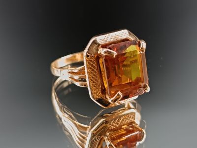 une photo d'une bague ornée d'une pierre orange posée sur une surface réfléchissante