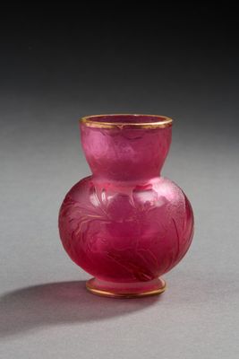 un vase en verre rose à bord doré posé sur une surface grise