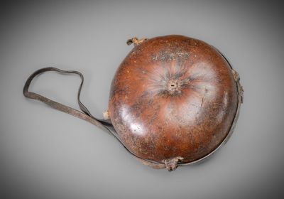 un vieux sac à main en cuir muni d'une poignée métallique, sur un fond gris