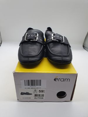 chaussures en cuir noir avec des boucles, posées sur une boîte, sur une surface blanche