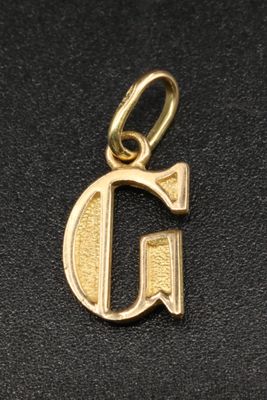 un gros plan sur une breloque en or sur laquelle figure la lettre « g »