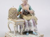 une figurine représentant une femme assise sur une table, avec une cage à oiseaux