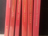 six livres rouges posés sur une étagère blanche, près d'un mur noir