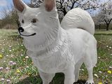 statue of a white dog standing in a field of flowers