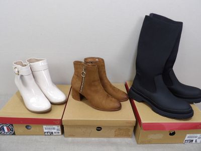 trois paires de bottes sont posées sur des cartons posés par terre