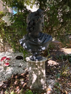 a statue of a man sitting on a pedestal in a garden