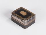 une petite boîte noire et dorée posée sur une surface blanche