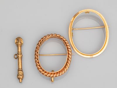 deux broches en or et une épingle posées sur un fond gris
