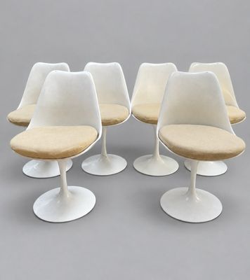 four white tulip chairs with beige cushions on a grey surface