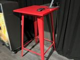 a small red table with a laptop on it in front of a black curtain