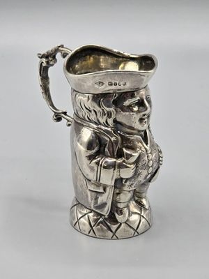 un pichet ancien en argent sur lequel est représenté un homme coiffé d'un chapeau