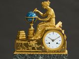 a gold clock with a woman sitting on top of it