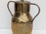 a brass pitcher with a handle on a white surface