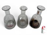 three empty glass bottles sitting next to each other on a white surface